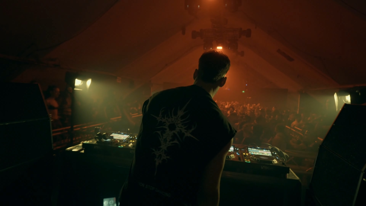 DJ pušta haus set pred punim klubom uz prigušeno svetlo i publiku koja igra ispred bine