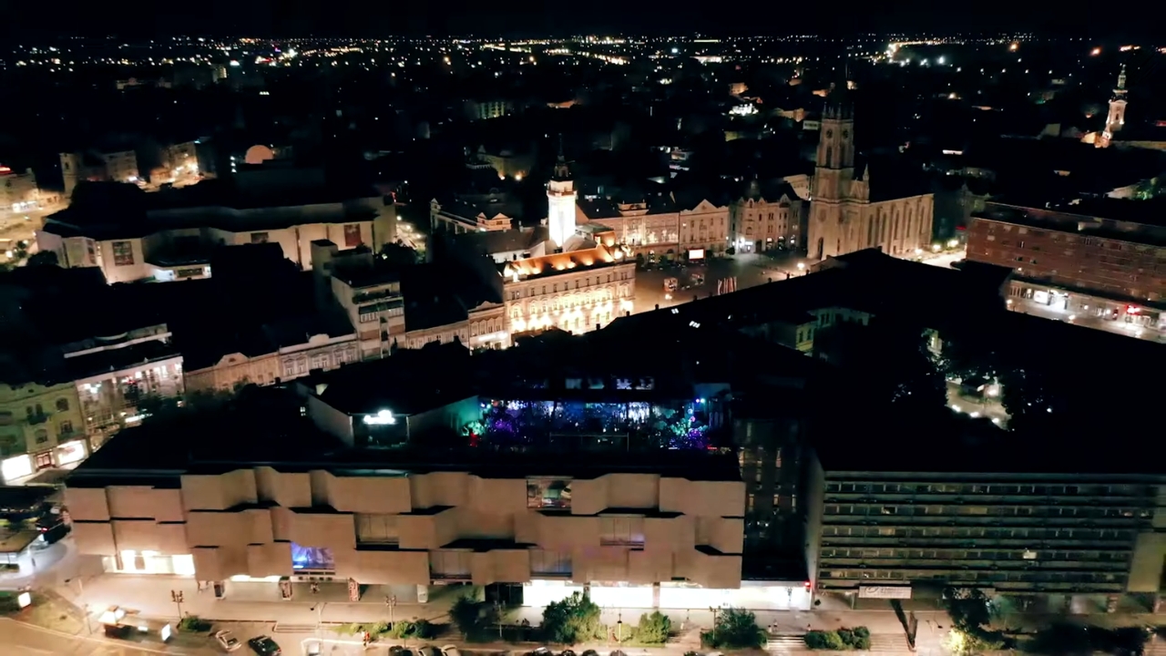 Pogled na Novi Sad sa osvetljenim centrom grada i punim klubom na krovu